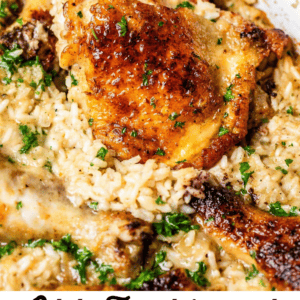 wooden spoon holding up a browned chicken thigh in a casserole dish with rice.