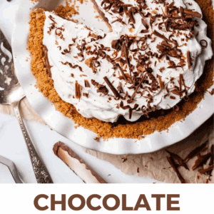 A chocolate cream pie with a graham cracker crust, topped with whipped cream and chocolate shavings, sits in a white pie dish with a slice missing. Text below reads “Chocolate Cream Pie Dessert – The Food Charlatan.”.
