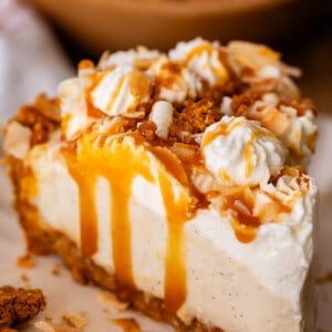 coconut cream pie on a plate with caramel drizzle and whipped cream and graham topping.