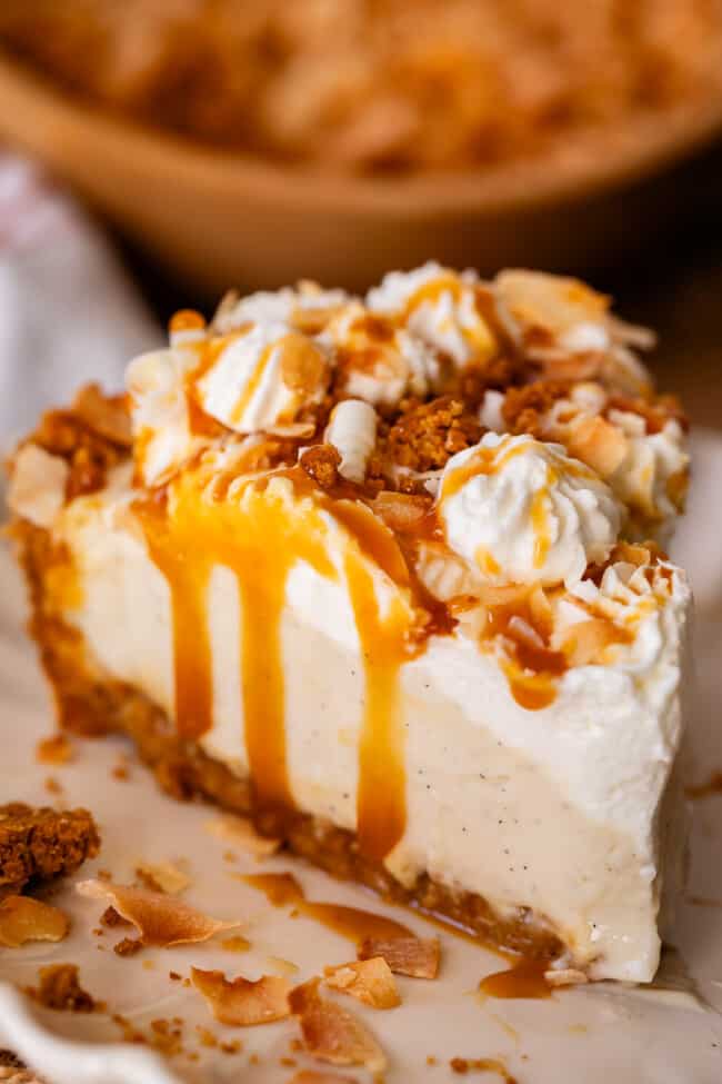 coconut cream pie on a plate with caramel drizzle and whipped cream and graham topping.