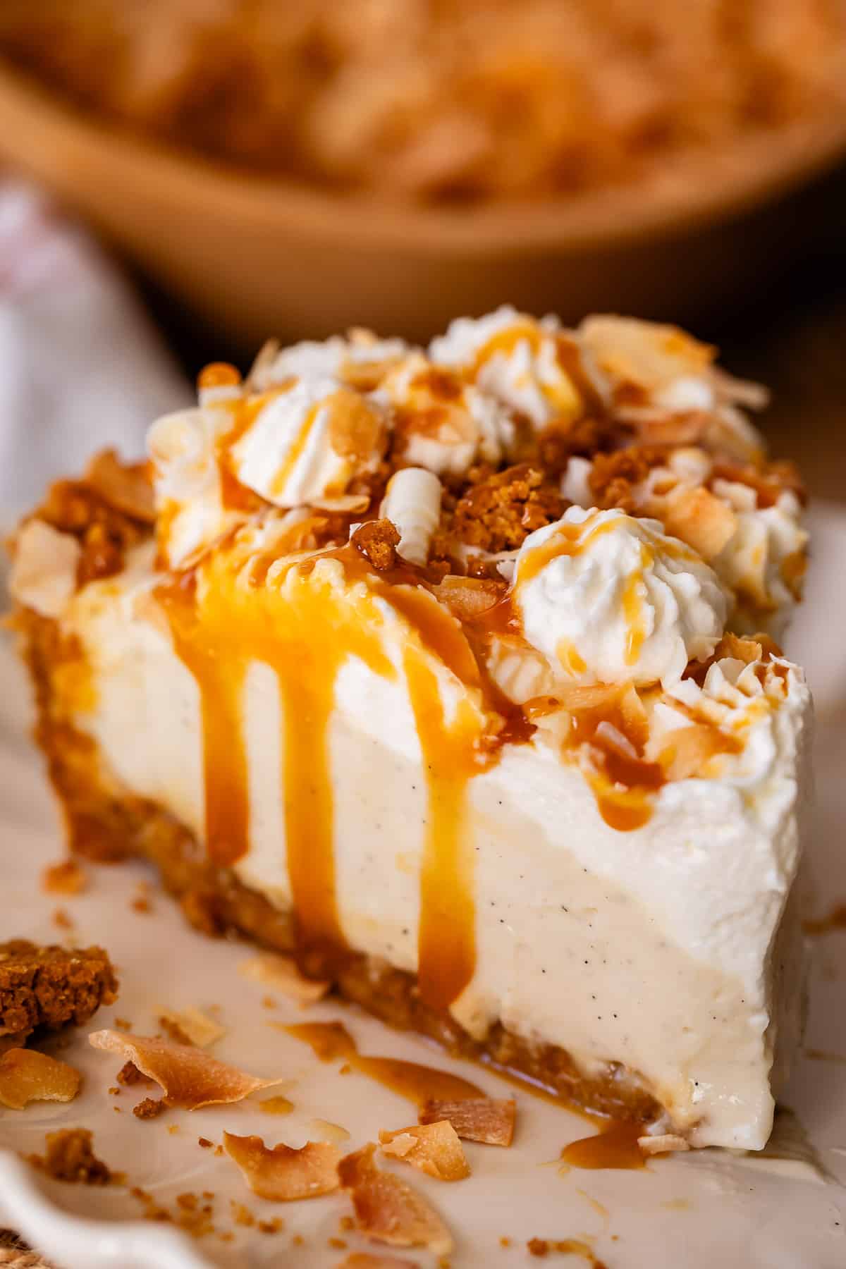 perfecltly sliced piece of coconut cream pie with whipped cream and caramel dripping down the side.