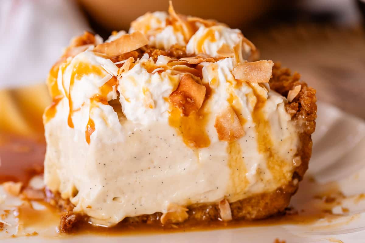 coconut cream pie on a plate from the side with caramel on the plate.