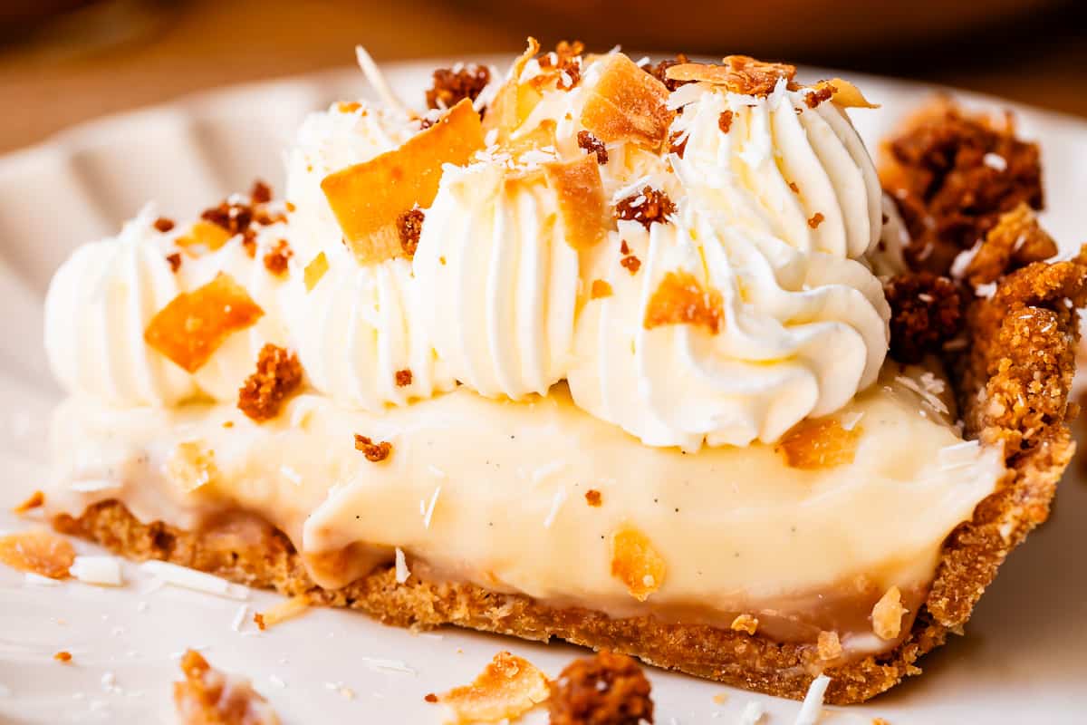 slice of coconut cream pie on a plate with whipped cream topping and toasted coconut.