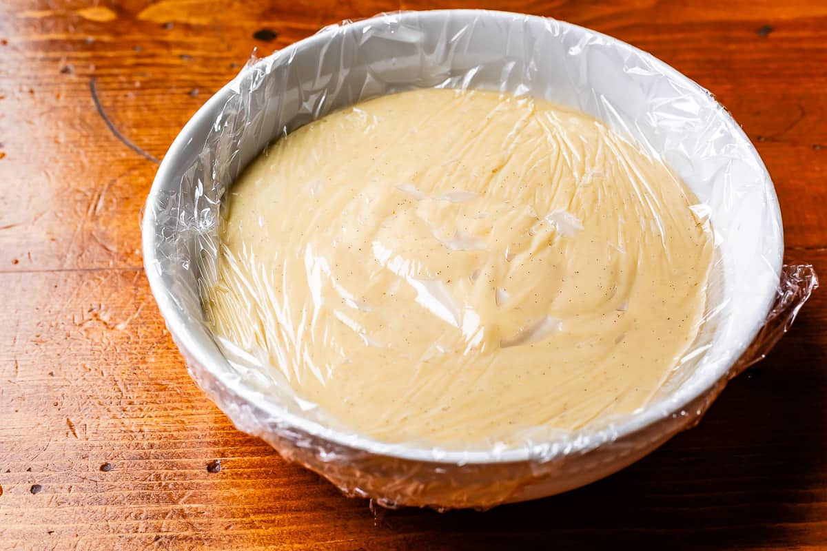 plastic wrap pressed directly up against coconut custard in a ceramic bowl.