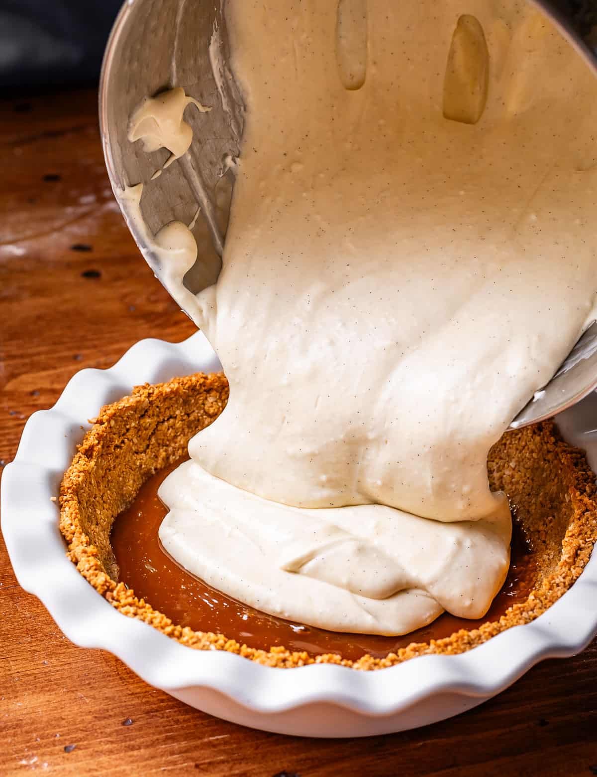 pouring whipped cream and coconut custard mixture into pie dish over caramel and crust.