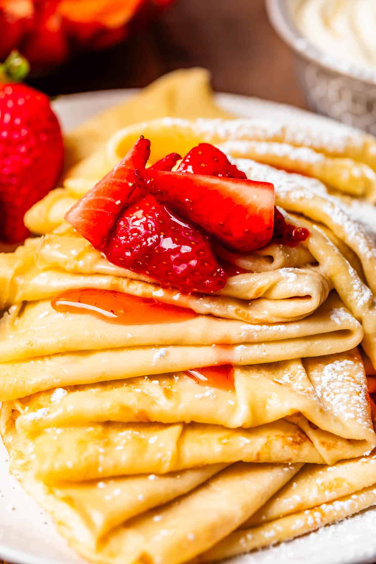 several folded crepes topped with powdered sugar and a ladle of macerated strawberries.