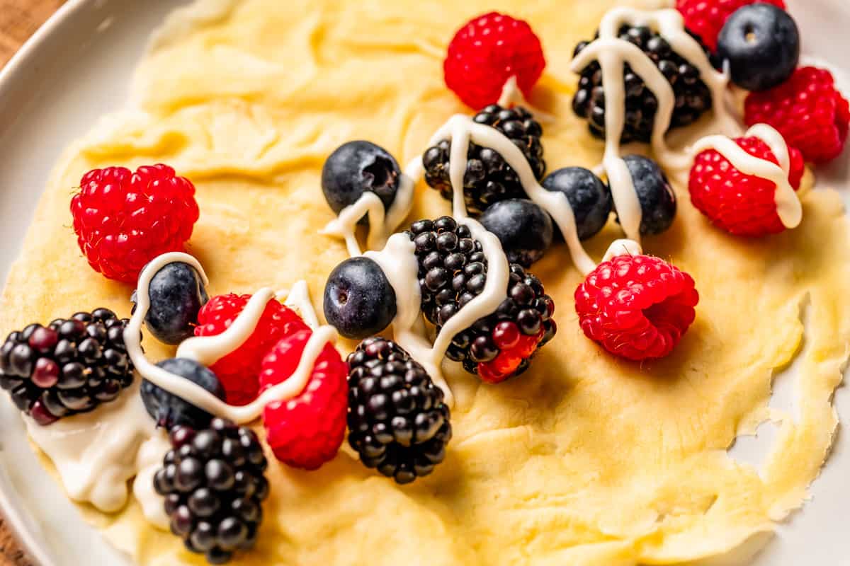 crepe on a plate topped with mixed berries and a drizzle of the cream cheese spread.