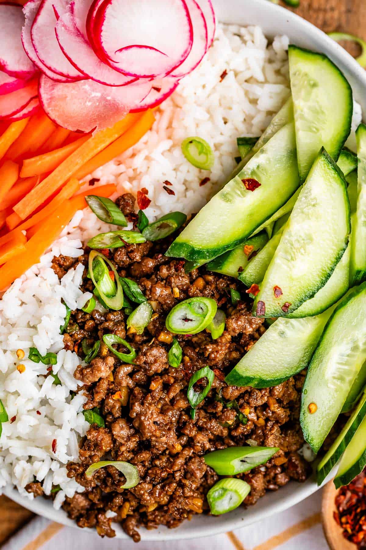 rice in a bowl topped with Korean beef, sliced cucumbers and radishes, and matchstick carrots.