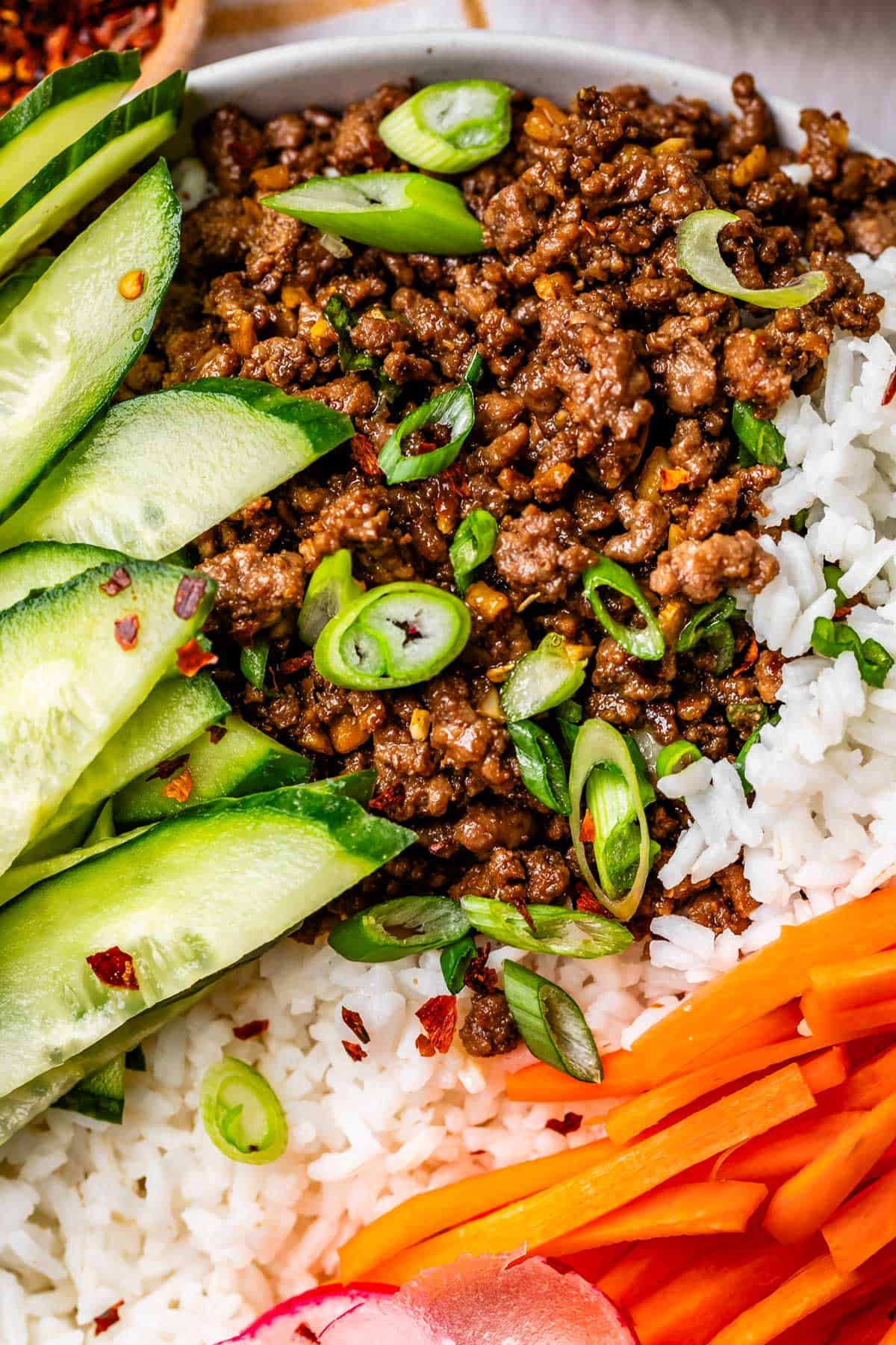 bowl with Korean beef, rice, cucumber slices, and matchstick carrots.