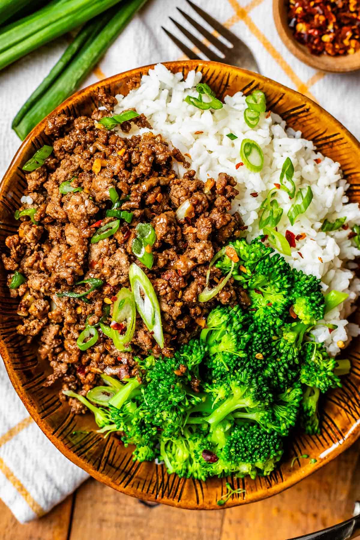Brown ceramic bowl filled with rice, broccoli, and Korean beef with green onion garnish. this one for hero? what do you think?