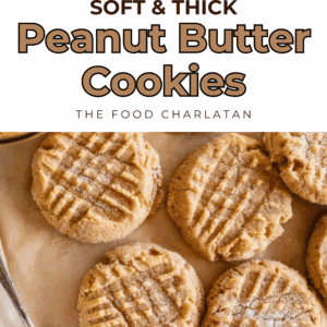 Overhead view of several soft & thick peanut butter cookies with classic crisscross fork marks on parchment paper, next to a spoonful of peanut butter. Text reads: “Soft & Thick Peanut Butter Cookies – The Food Charlatan.”.