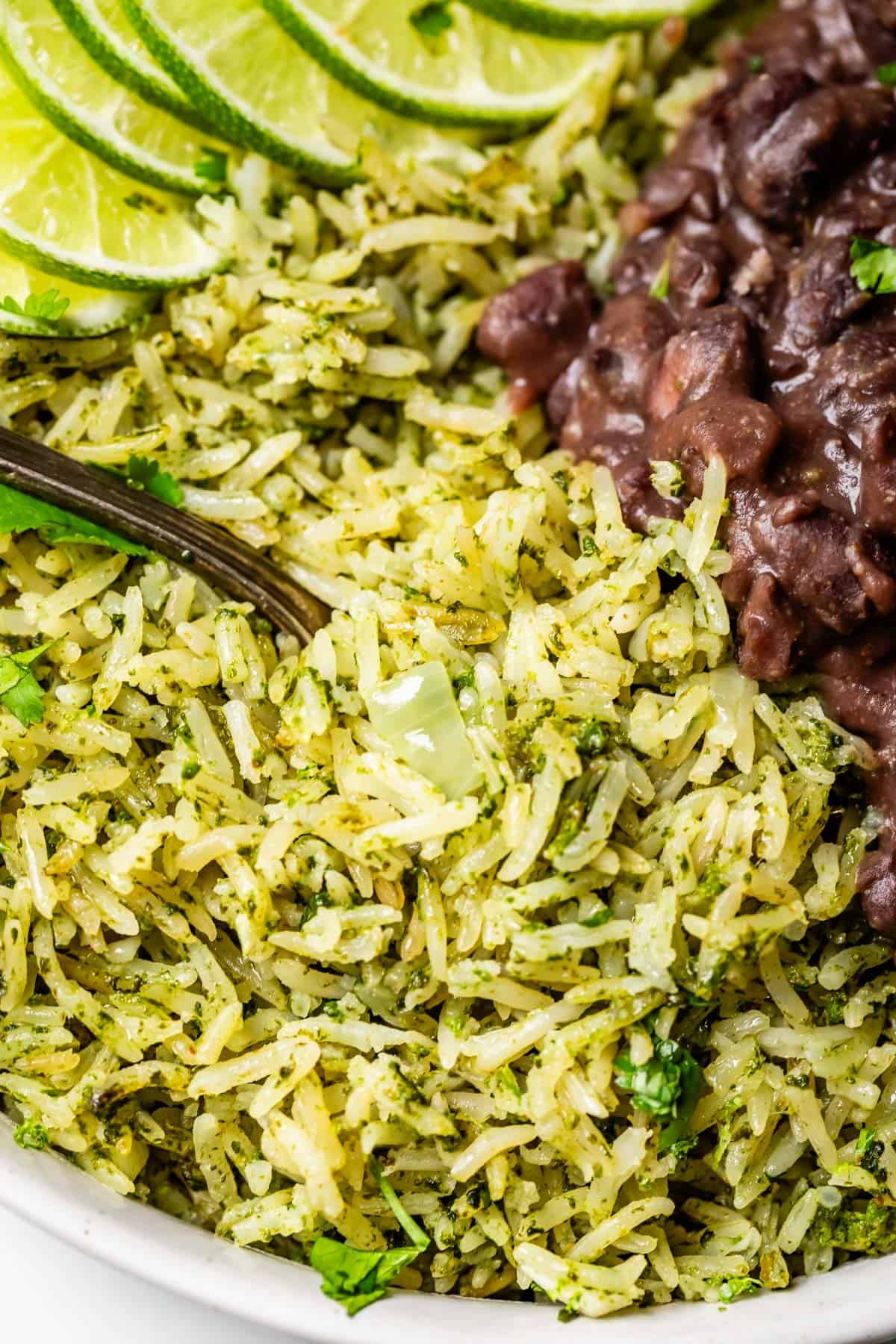 close up of green cilantro lime rice with lime garnish and a side of black beans.