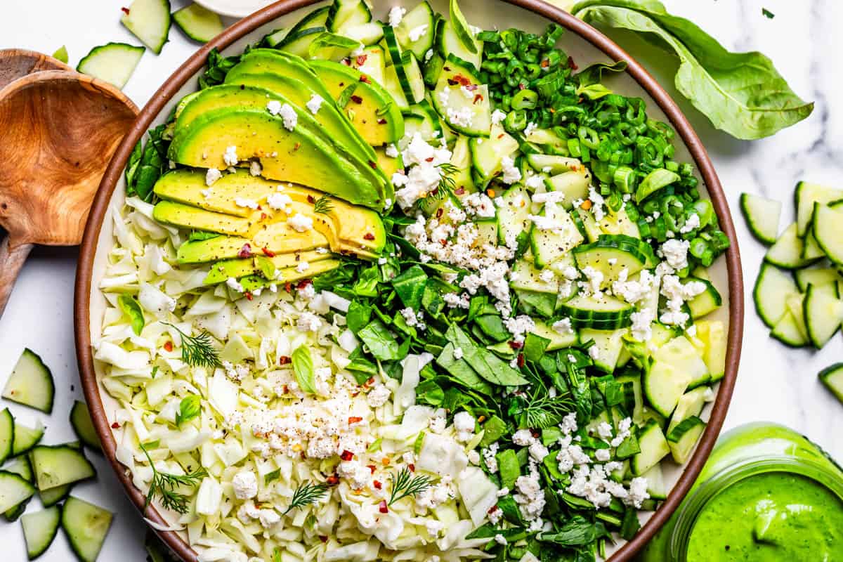 salad with cabbage, spinach, cucumber, green onion, avocado, and feta on a ceramic plate.