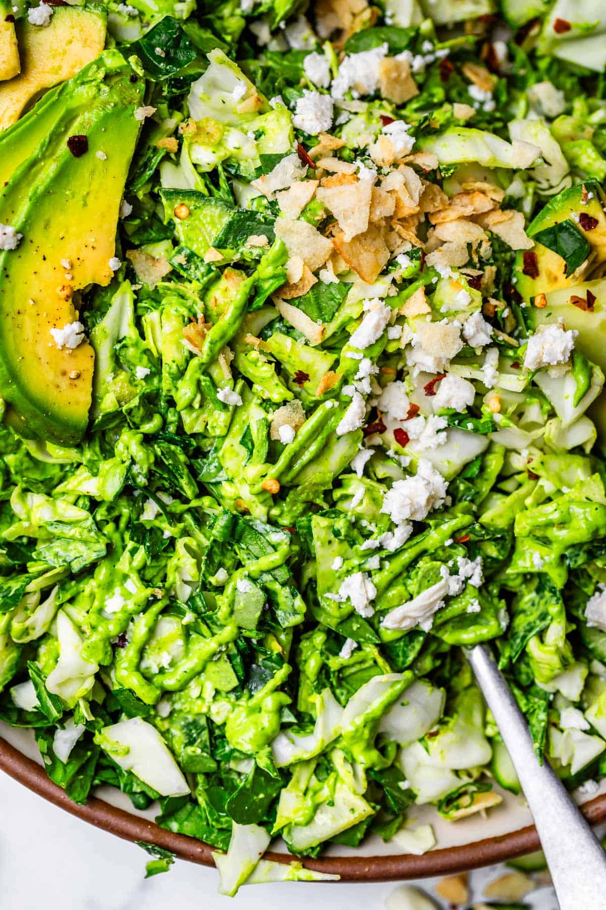 fork digging into green goddess salad with avocado and feta cheese on top.