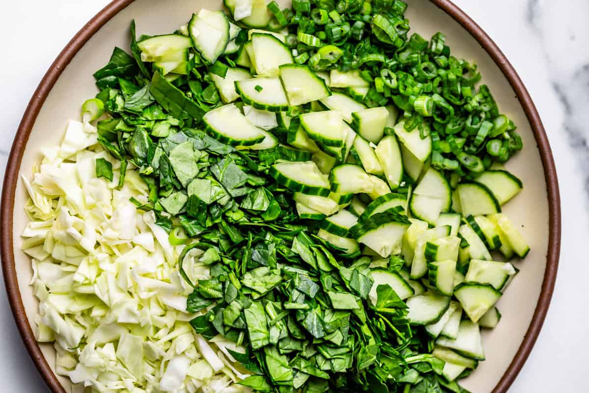 finely chopped cabbage, spinach, cucumber, and green onion on a ceramic plate.