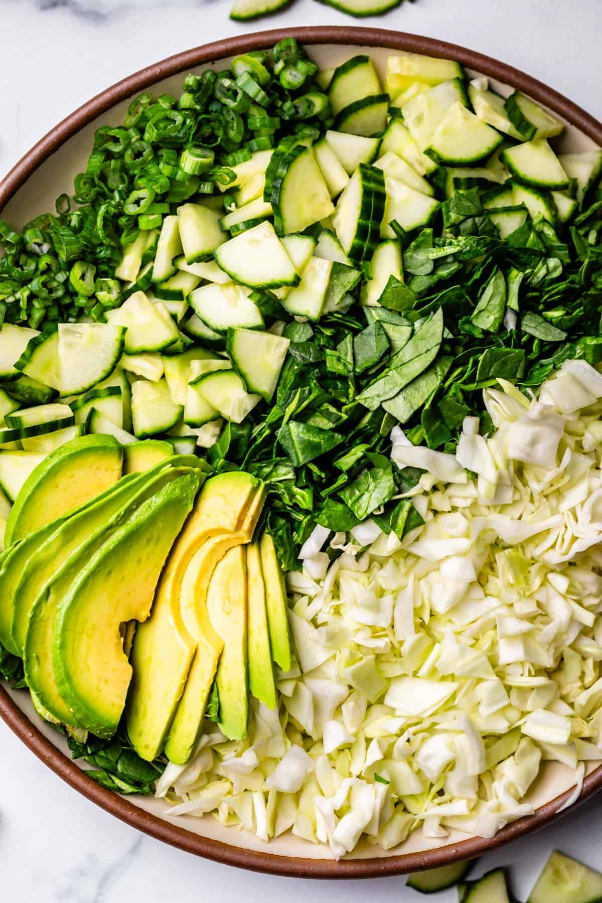 chopped green onion, cucumber, spinach, cabbage, and avocado lined up on a plate.