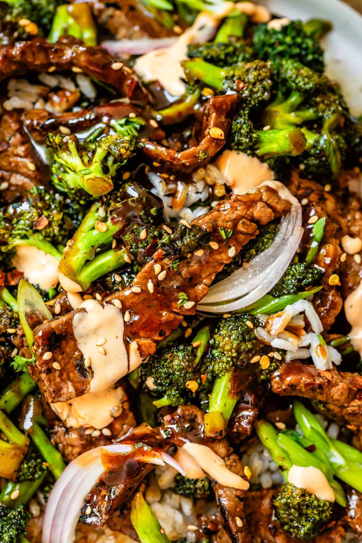 Beef and broccoli close-up with rice, onions, and sriracha mayo.