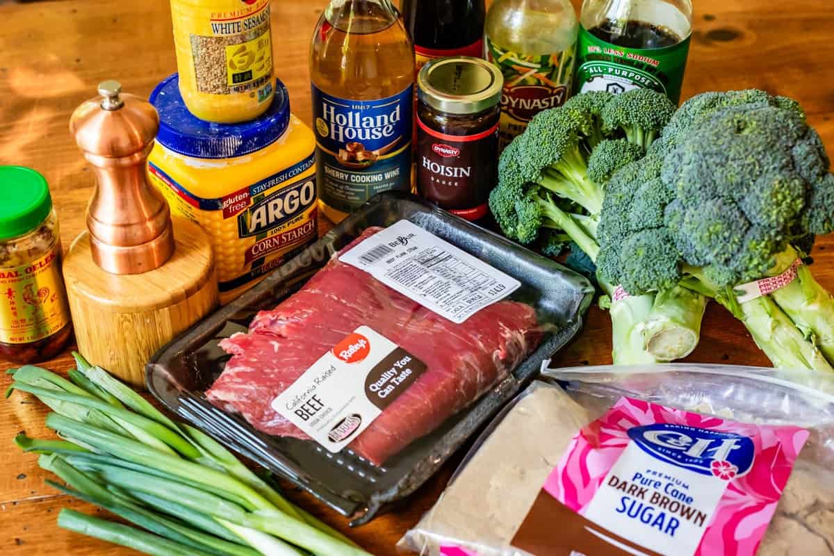 ingredients laid out on a table, including flank steak, brown sugar, broccoli, hoison sauce, salt, sherry wine.