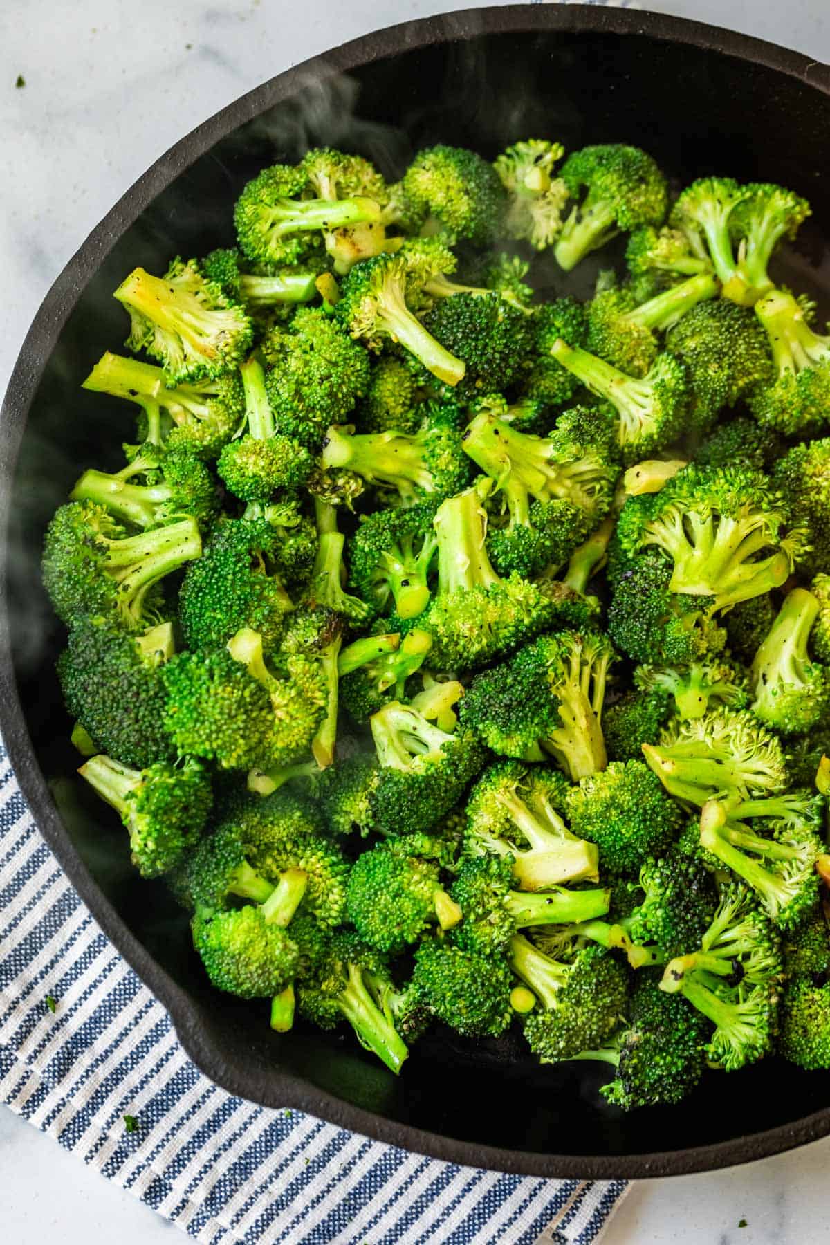 overhead shot of stir frying broccoli in a cast iron skillet.