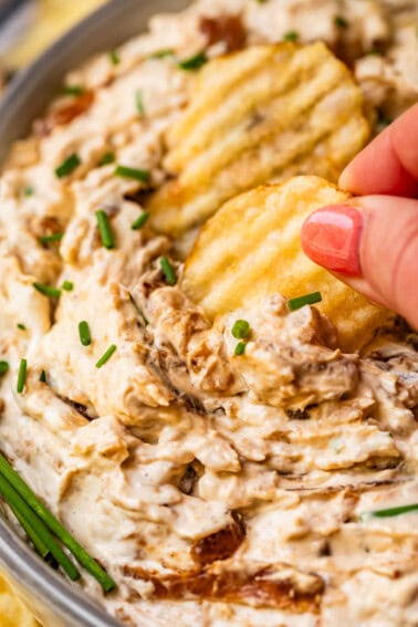 hand pulling crinkle cut potato chip scooping up french onion dip.