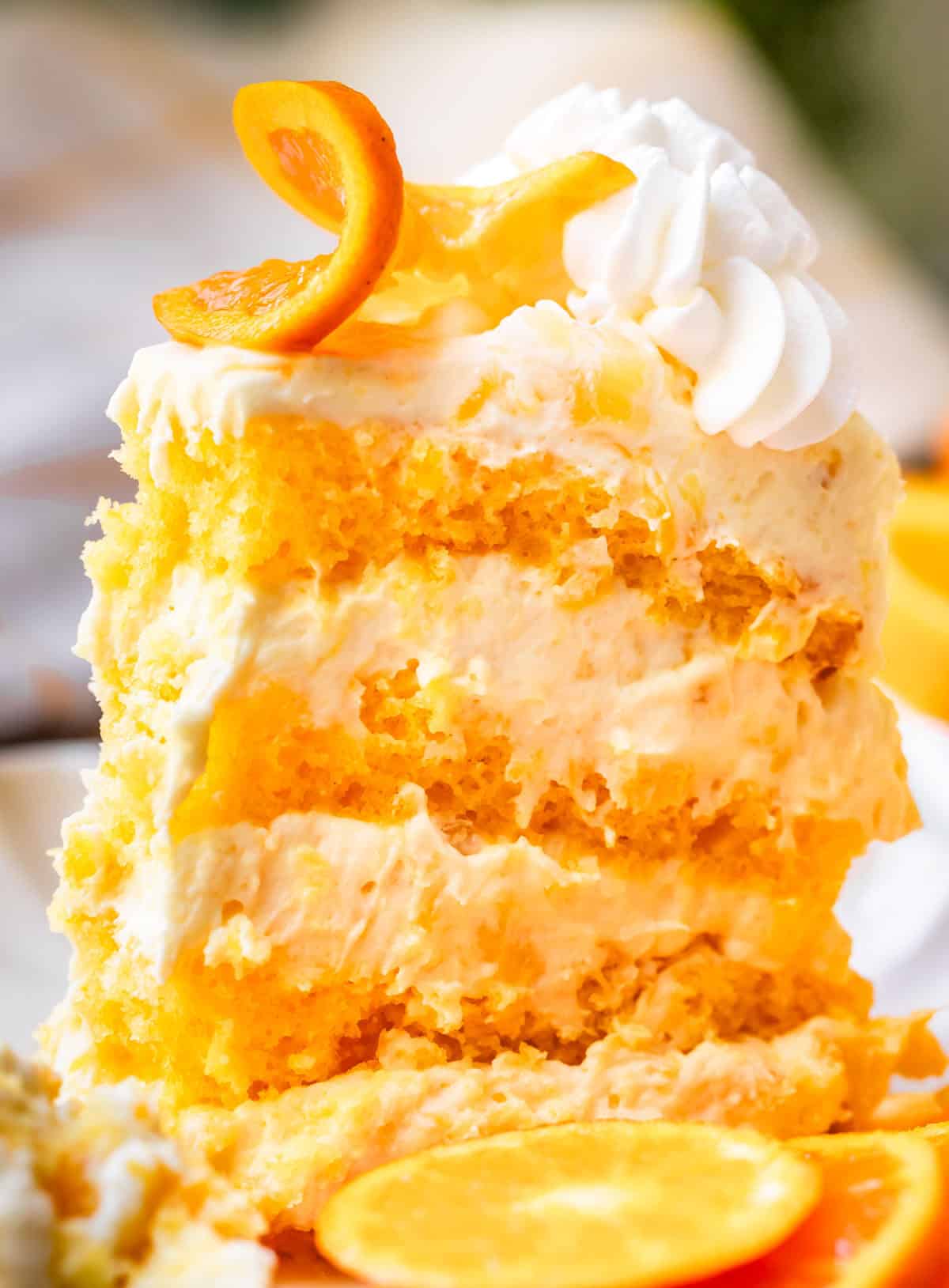 side view of a tall piece of sunshine cake with 8 layers, garnished with an orange slice.