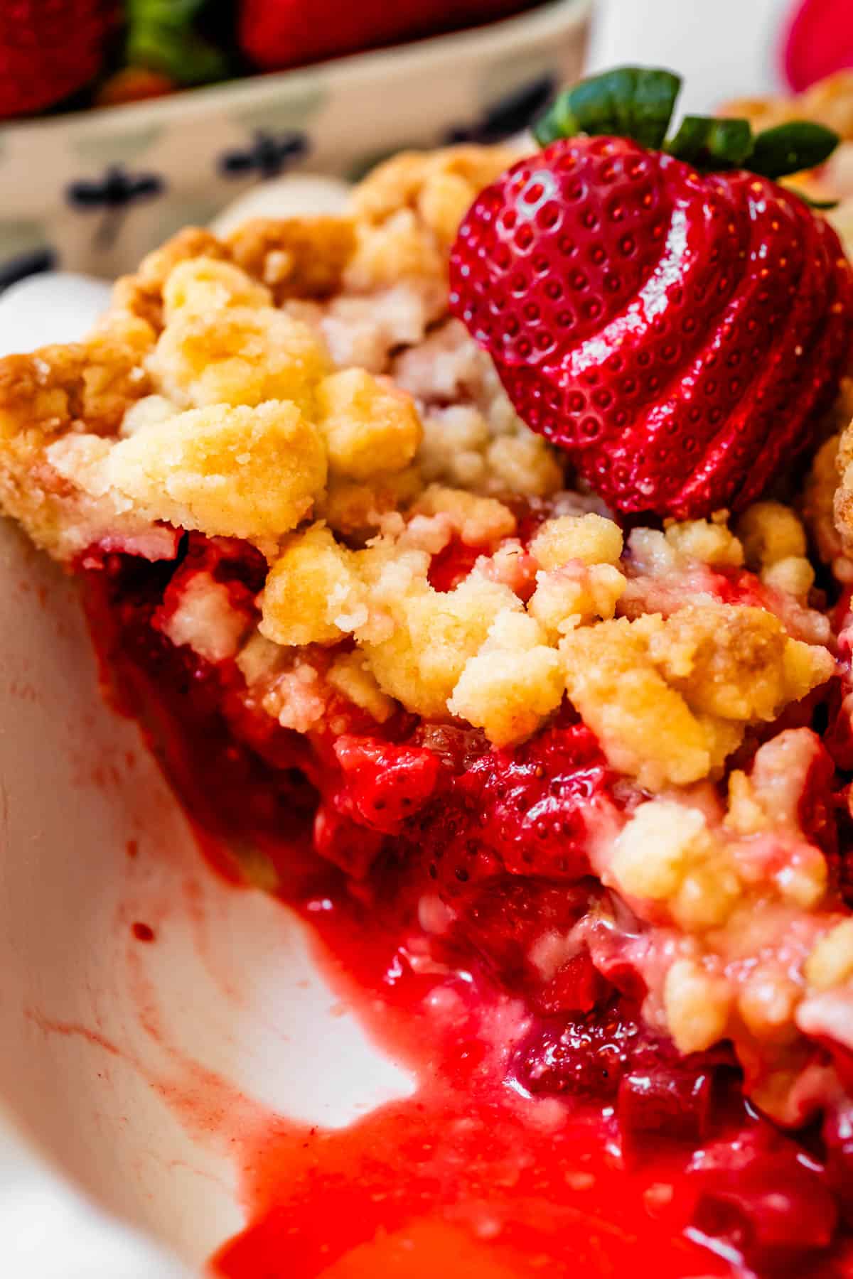 a slice of crumble topping strawberry rhubarb pie in a pie pan with strawberry slice garnish.