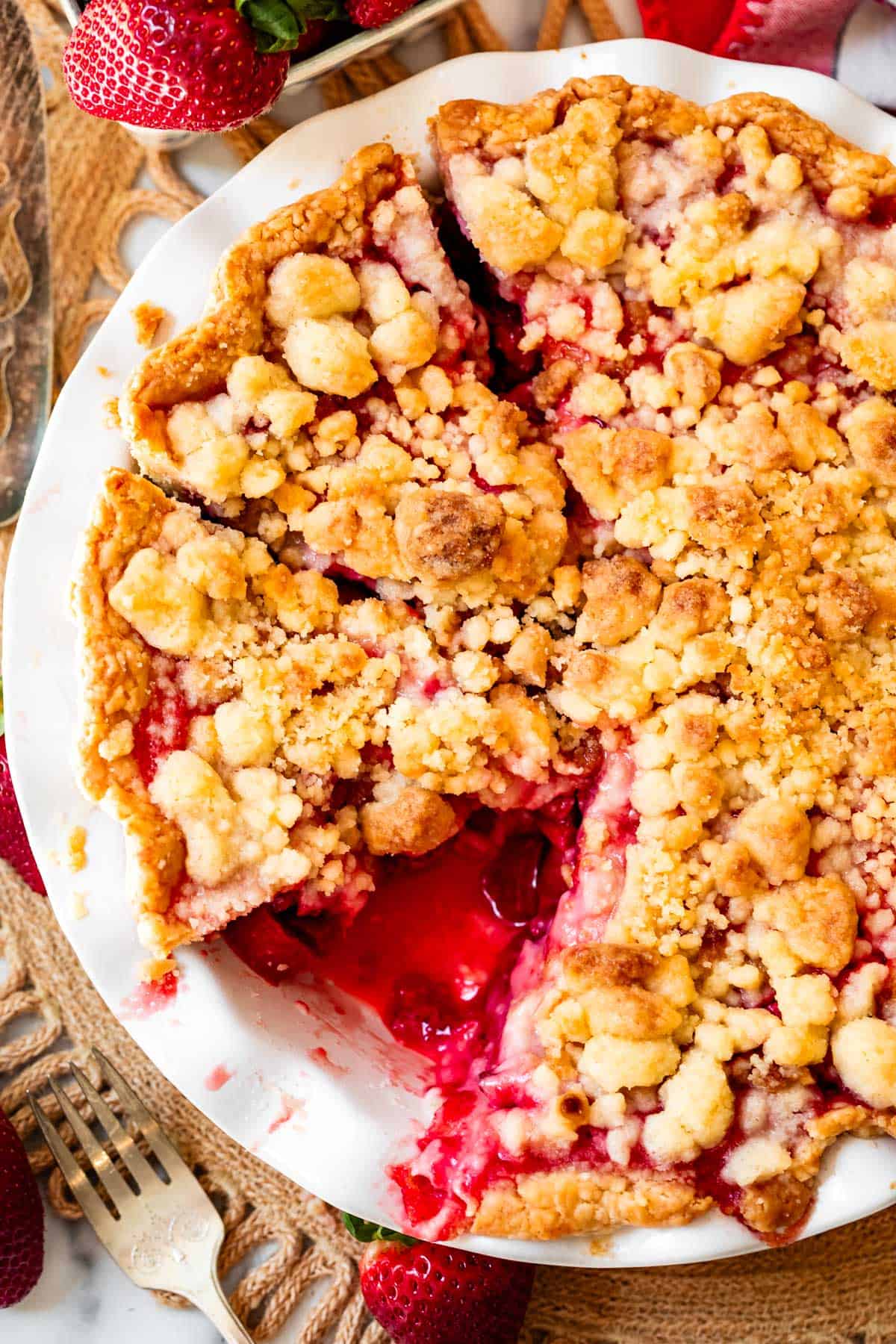 whole crumble topped rhubarb strawberry pie with slices cut and one removed from pan.