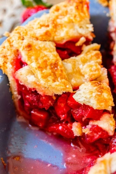 piece of lattice crust rhubarb and strawberry pie with lots of filling in a pie pan.