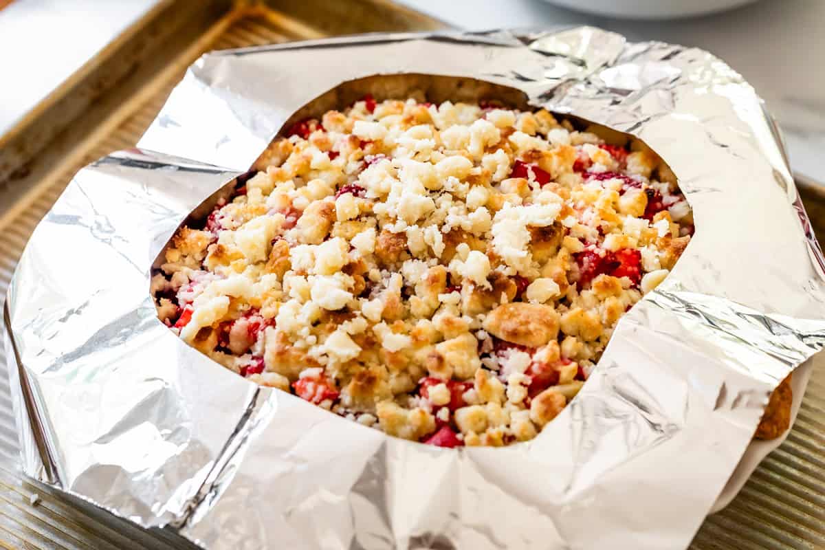 strawberry rhubarb pie with crumble topping with crust protected by a foil shield.
