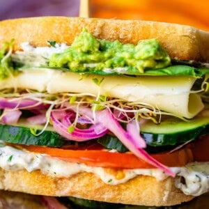 sideways view of a veggie sandwich with cheese showing all the layers and a skewr in the top.