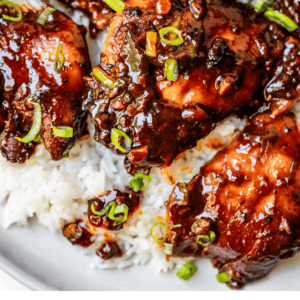 Several chicken thighs on a plate of white rice, garnished with green onions.