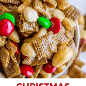 Close-up of Christmas Chex Mix with cereal squares, red and green candy-coated chocolates, and peanuts in a glossy, sweet glaze. White background features CHRISTMAS CHEX MIX and THE FOOD CHARLATAN text below.