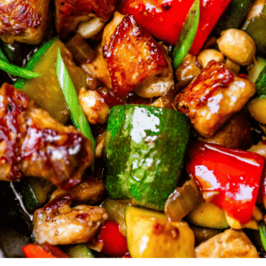 Pin image of kung pao chicken close up with chunks of perfectly searched chicken and veggies.