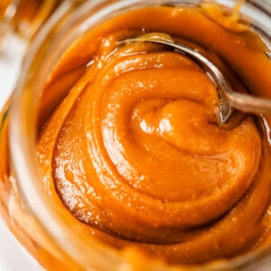 metal spoon digging into salted caramel from a glass mason jar.
