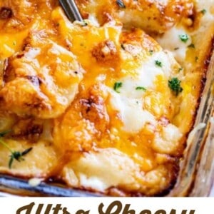 A close-up of a casserole dish filled with golden, ultra-cheesy mashed potatoes, topped with melted cheese and parsley, sits with a serving spoon. Text below reads, Ultra Cheesy Make-Ahead Mashed Potatoes - The Food Charlatan.