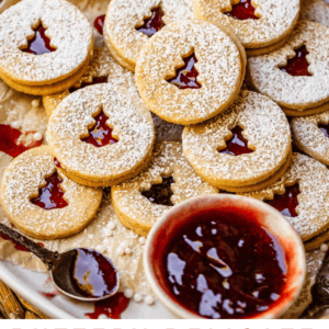 plate of over a dozen linzer cookies with christmas cut outs and jam.