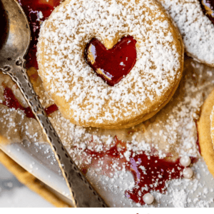 heart shaped linzer cookies with raspberry jam and metal spoon.