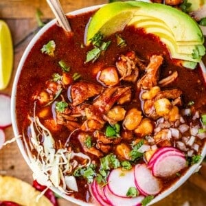 bowl on a wood table filled with pork, hominy, avocado, and more.