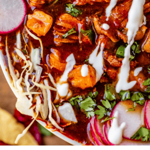 sour cream drizzled over posole in a white bowl with radishes.