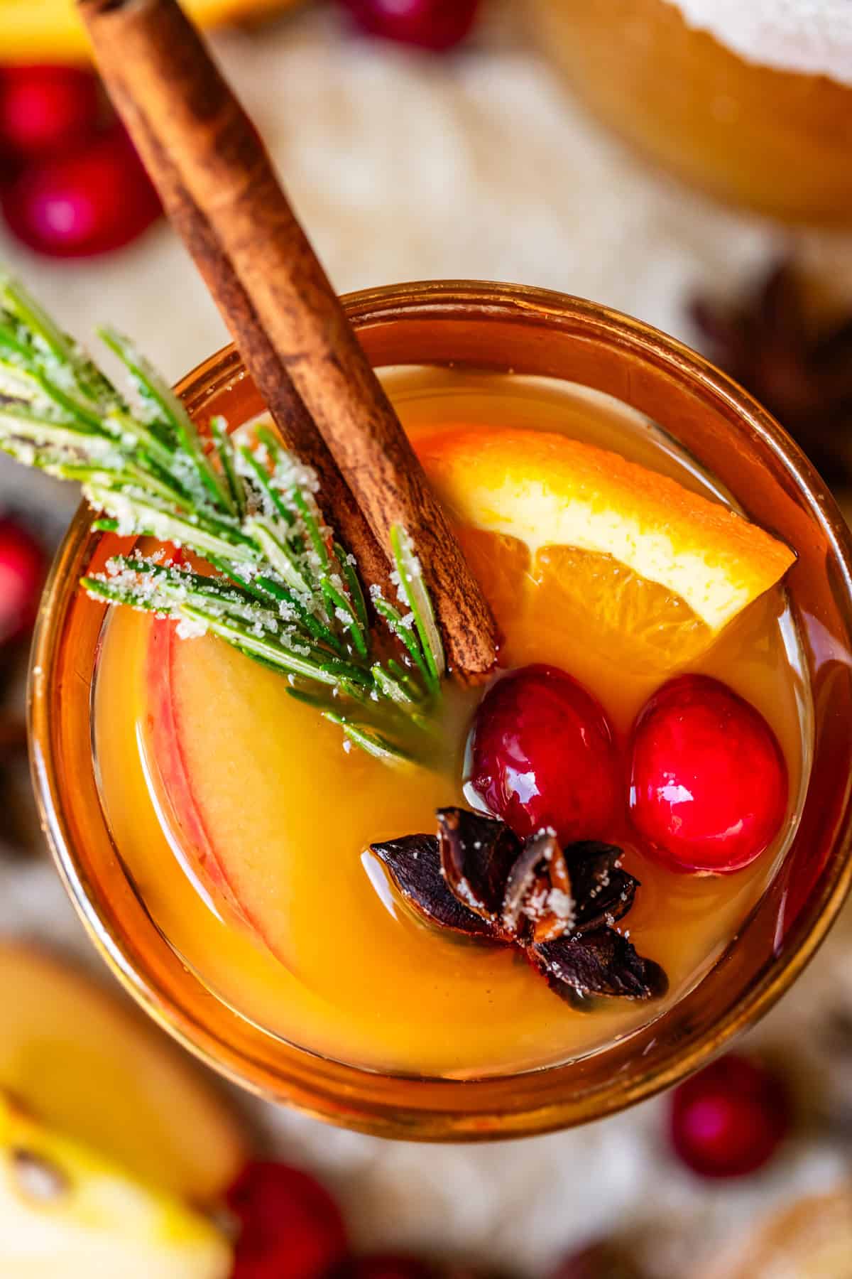 glass of wassail with orange, cranberry, and spice garnish on top.