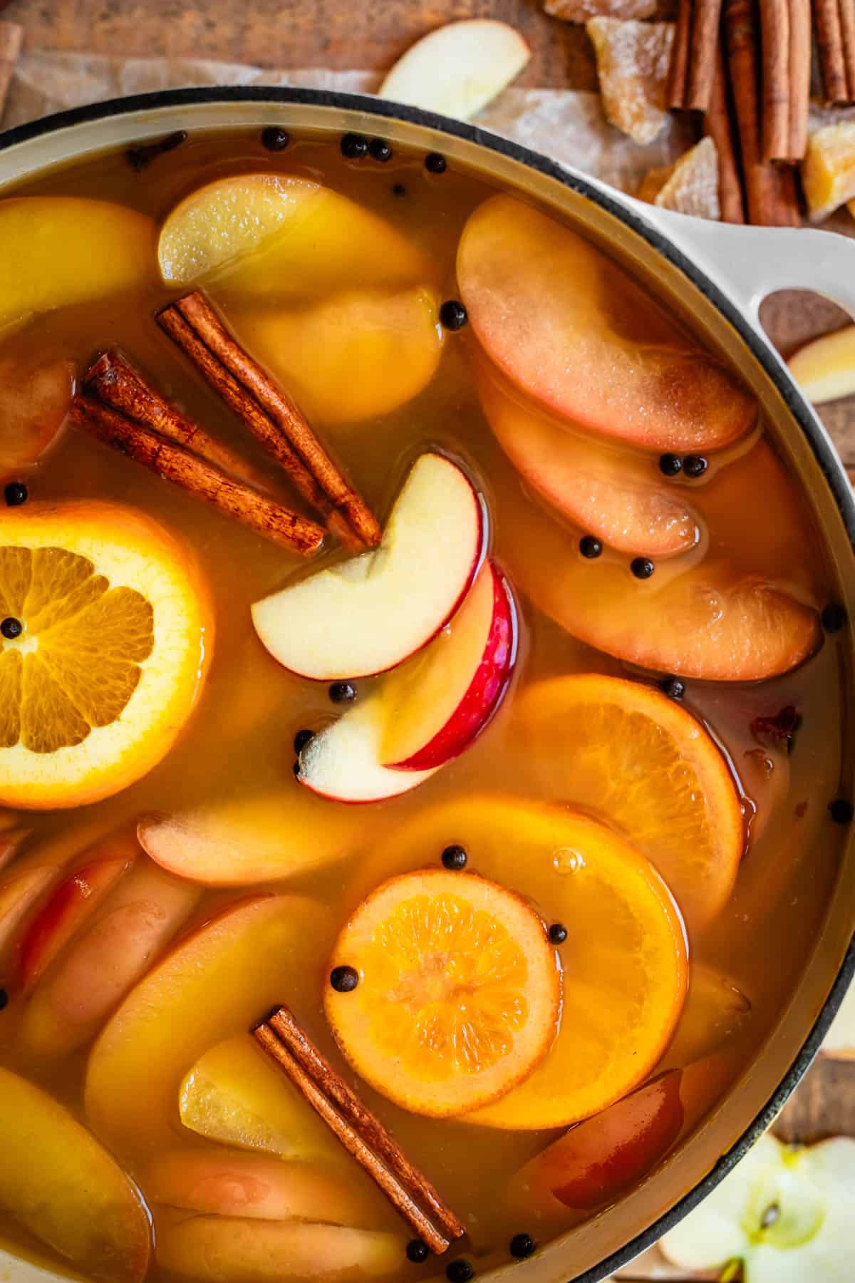 close up of a large pot filled with wassail, topped with fruit slices and cinnamon sticks.