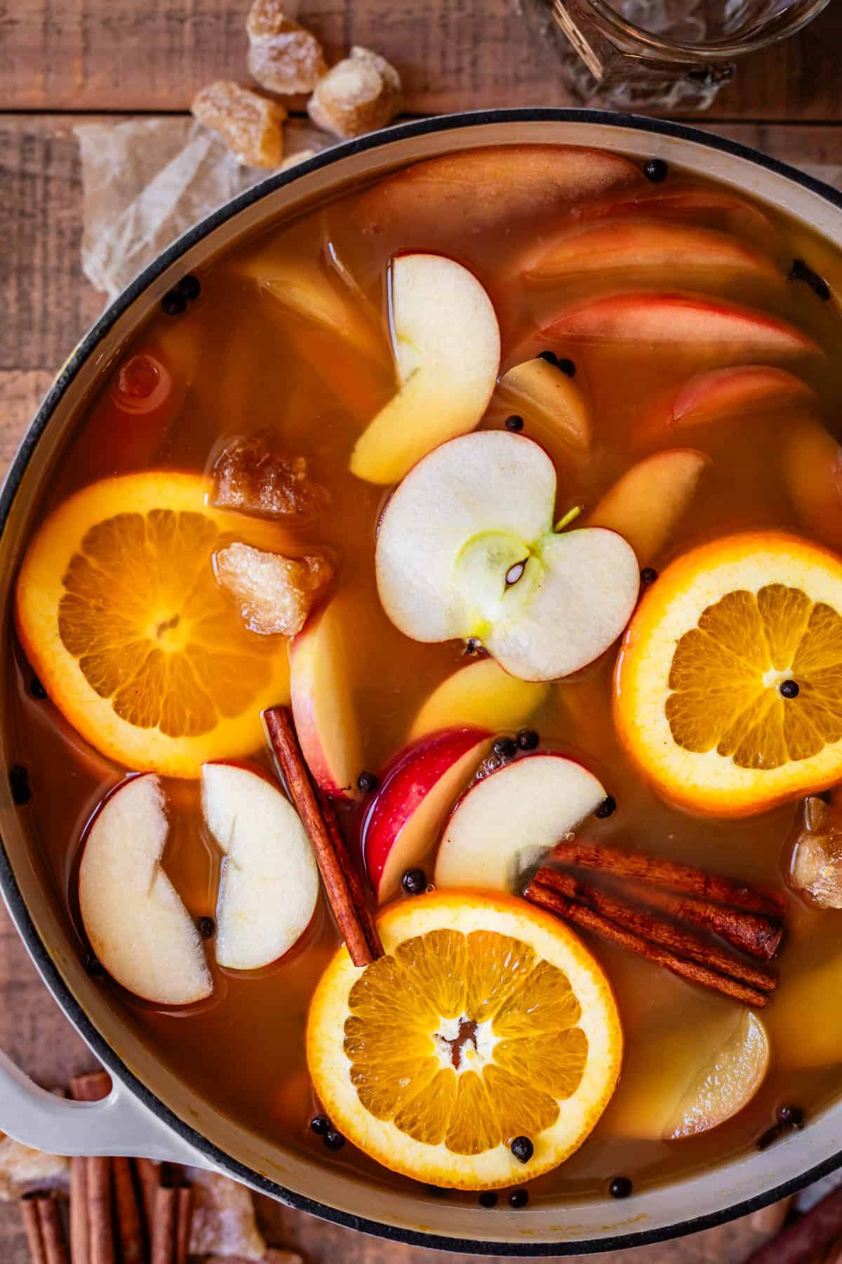 looking down into a pot with orange and apple slices and spices floating in wassail.