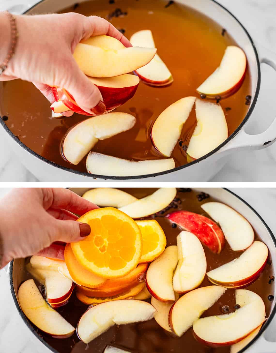 hand adding slices of apples and oranges to the wassail in the pot.