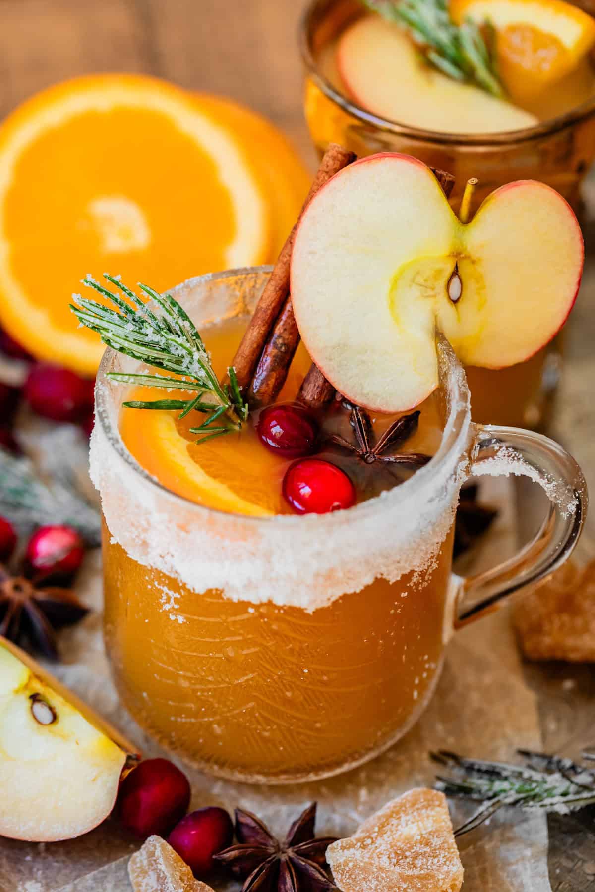 sugar rimmed glass mug of wassail with apple, spice, and sugared rosemary garnish.