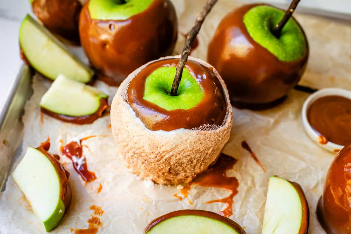 caramel apple dipped in white chocolate and cinnamon sugar, with plain caramel apples behind.