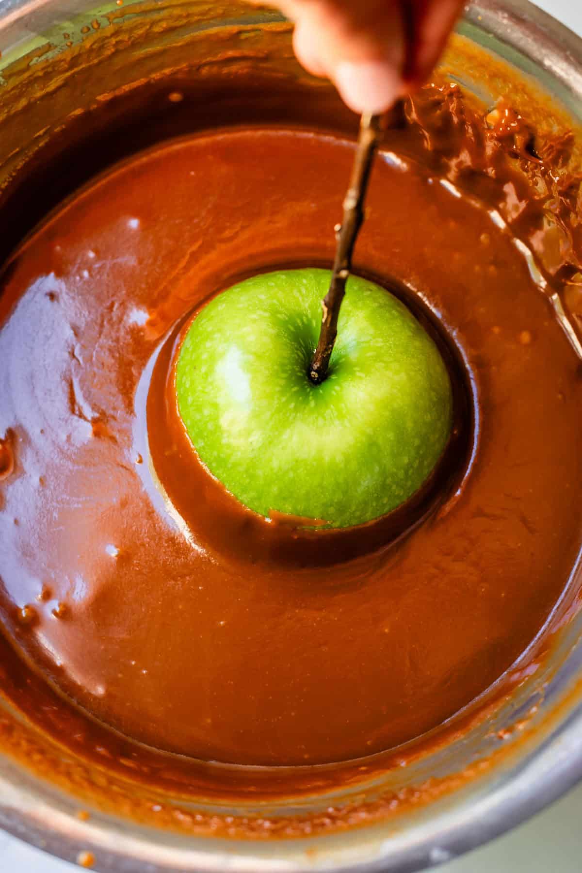 dipping a green apple on a stick in caramel in a pot.
