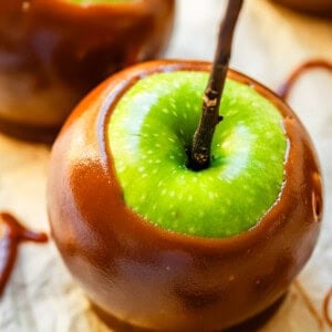 Green caramel apple with a stick in the center on parchment paper.