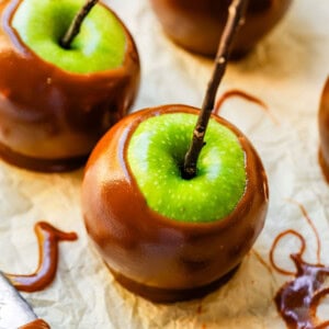 Green apple caramel apple with twig stick spoon of caramel nearby.
