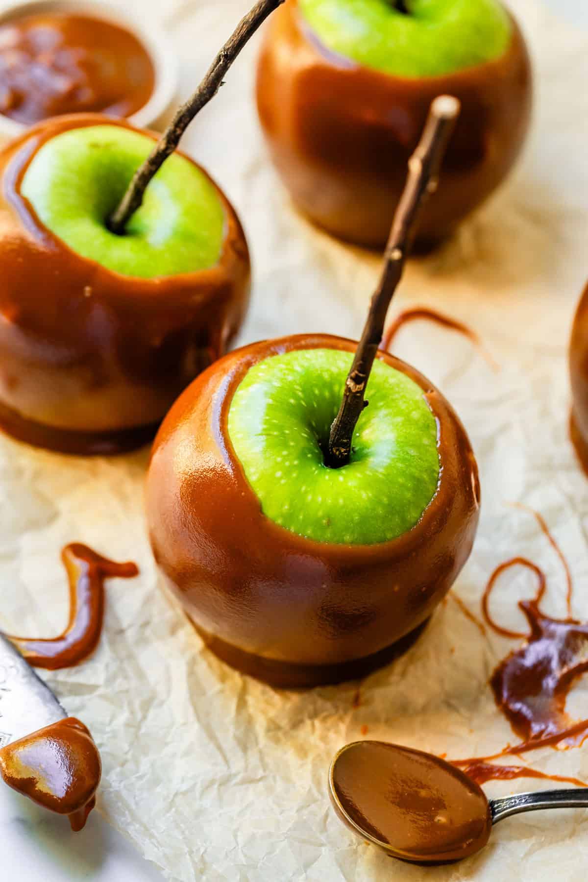 Green apple caramel apple with twig stick spoon of caramel nearby.