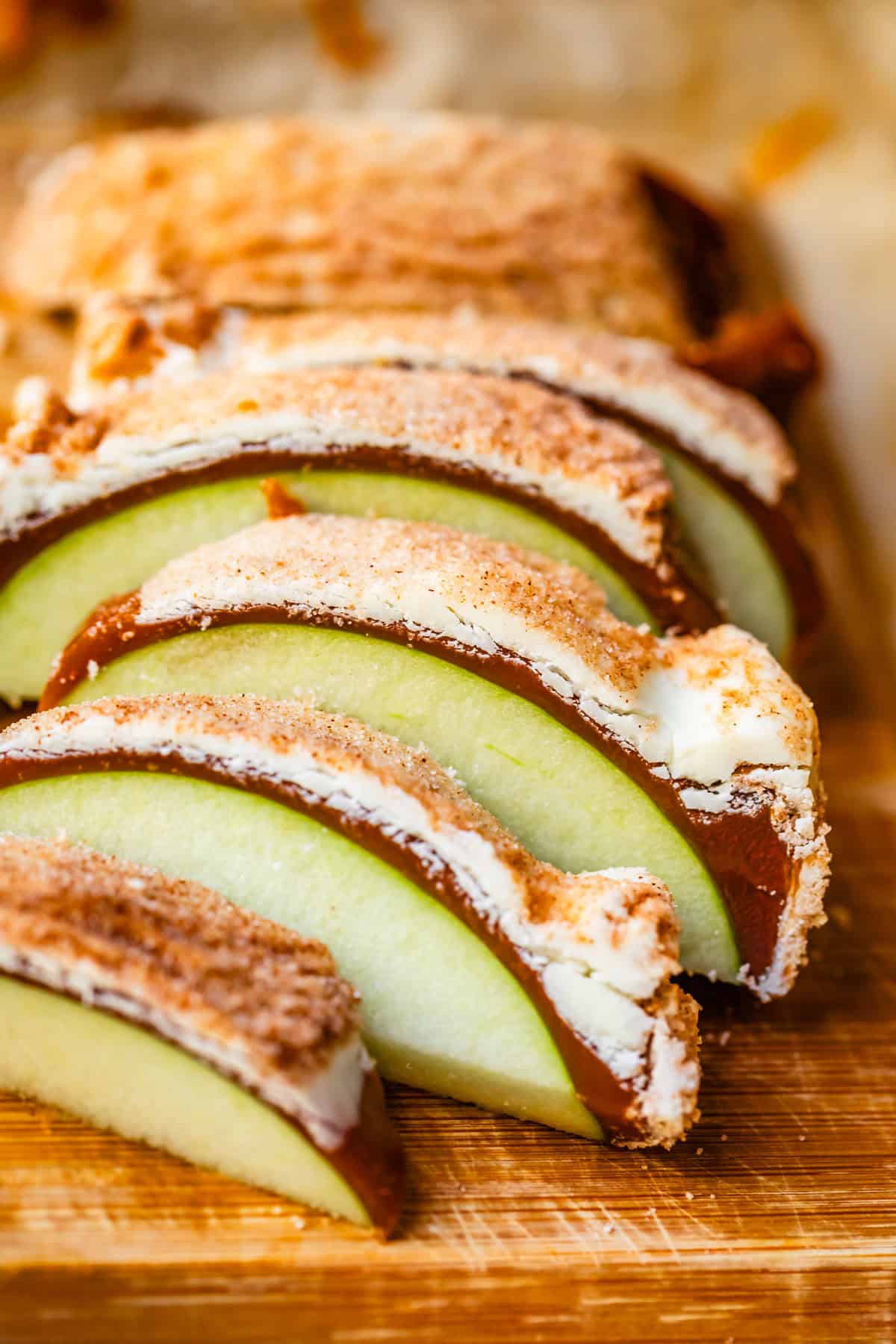 Slices of caramel apple covered in snickerdoodle coating on wood cutting board.